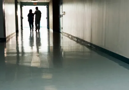 Two health care workers in a long hallway, one touching the other's shoulder