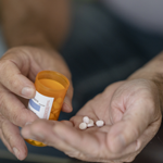 Close up of a caucasian man's hands holding and pouring pills.