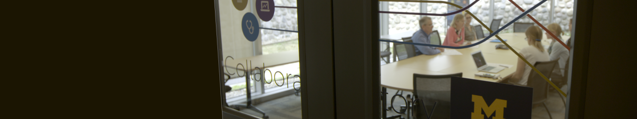 photo of five people sitting around a table in a conference room, view from outside the glass door