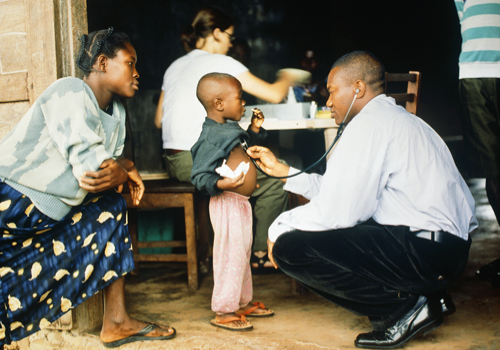 photo of a medical clinic in Africa, a doctor crouching down to listen to the heart of a young child
