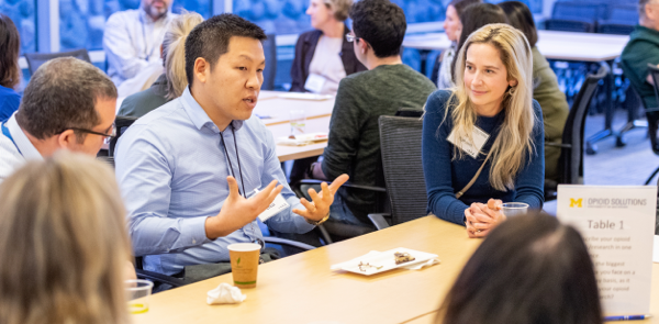 photo of 5 people seated at a table talking with each other at a conference