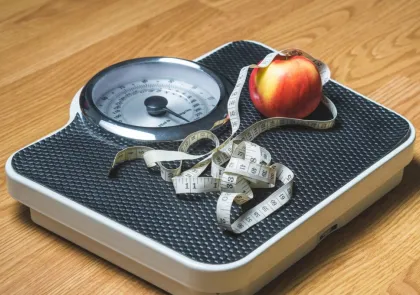A scale with a tape measure and an apple on it