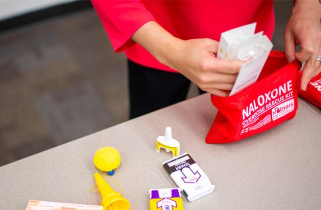 Hands reaching in a red bag labeled Naloxone