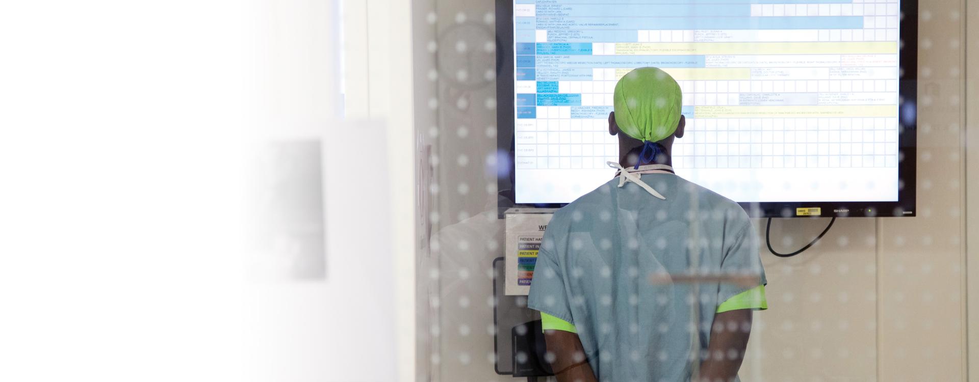 doctor in medical scrubs with their back turned looking at a wall mounted screen