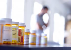 a collection of prescription medication bottles with a blurred background of a person in contemplation
