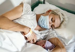 A mother with a mask holding a newborn baby in a hospital bed